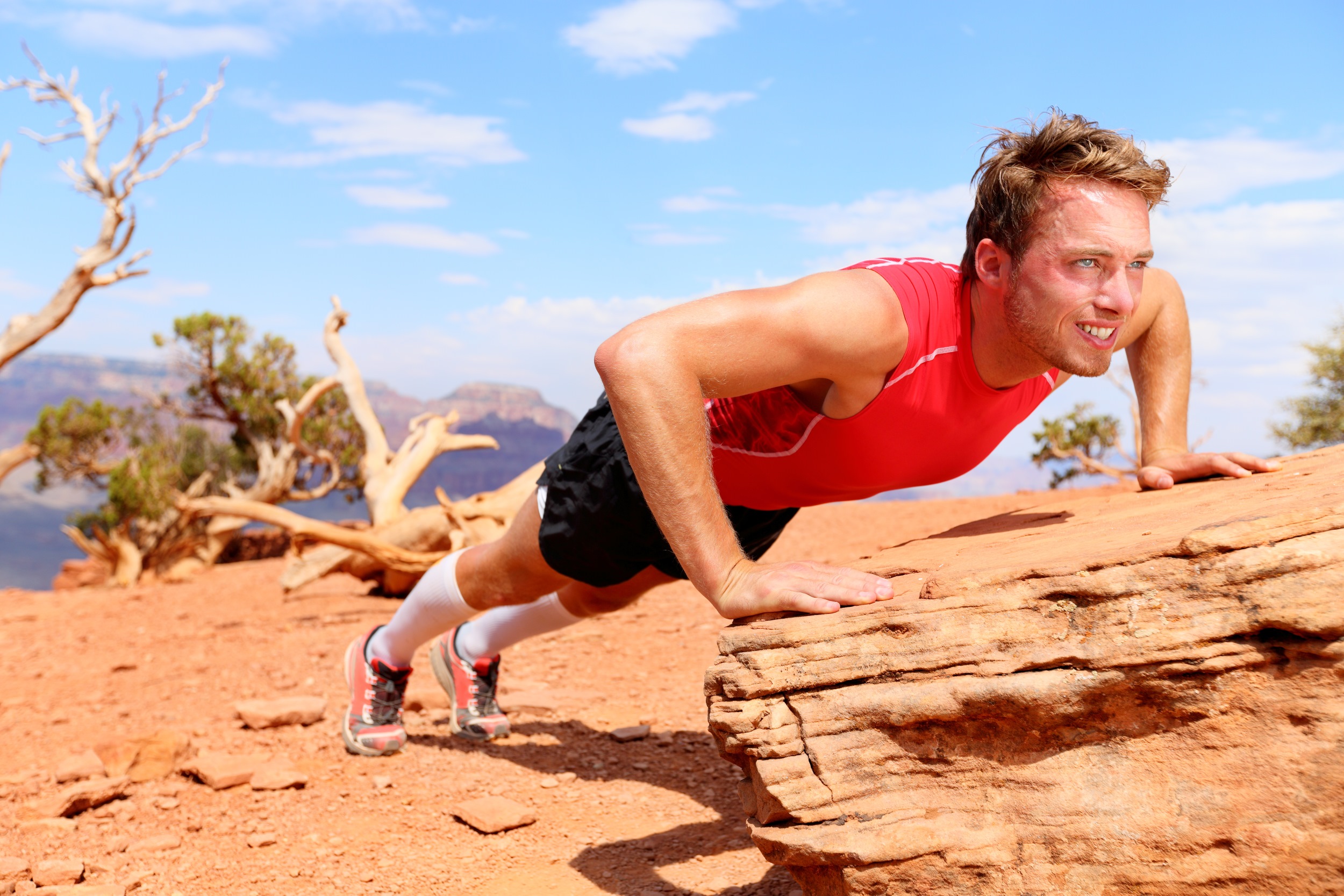 man red shirt outside blue sky doing incline push up on a log